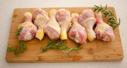 Chicken drumsticks on a cutting board with fresh rosemary and thyme. 