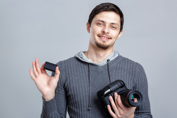 young smilling photographer in shirt  holds the battery for DSLR