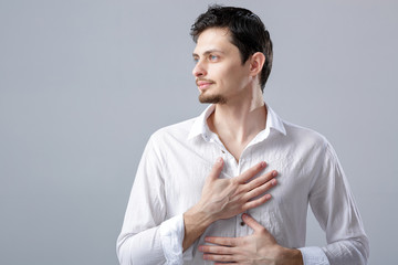 handsome young proud man in shirt holding hand on chest on grey 