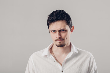 handsome young frustrated and resentful man in white shirt on gray background. soft, light