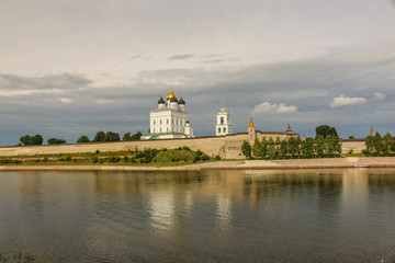 Fototapeta na wymiar Ancient old fortress on the river bank bright clouds sky July, Russia - Pskov Kremlin wall, Trinity Cathedral, Bell Tower and Dovmontova (Smerdya) tower at the sunset. View from the Velikaya river