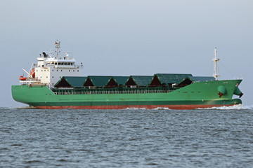 grünes Frachterschiff mit geöffneten Ladeklappen