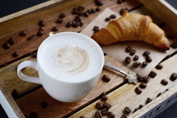 White cup of cappuccino and croissant on the wooden tray
