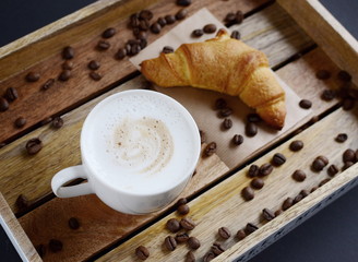 White cup of cappuccino and croissant on the wooden tray