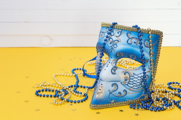 Venetian carnival blue mask with beads on a yellow background.