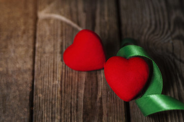 Valentines day background with two red hearts wrapped in green ribbon on rustic wooden background.Holidays card with copy space..