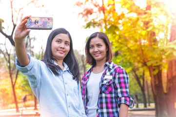 Portrait of a two young asia woman making selfie photo on smartphone in park of Thailand