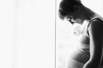 Young beautiful pregnant woman standing near window at home