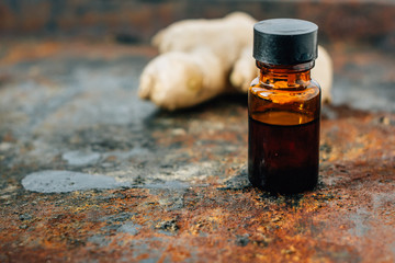 Ginger essential oil in glass bottle with ginger root behind.