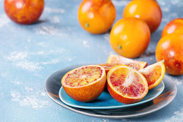 Sliced and whole ripe juicy Sicilian Blood oranges fruits on ceramic plate over blue concrete...