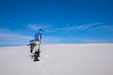 Man in blue cap with a snowboard climbs up the sand dune