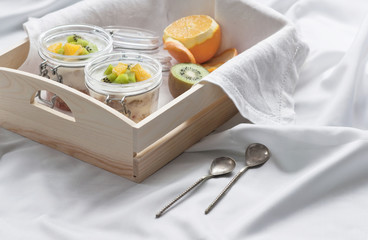 Healthy breakfast of muesli with yogurt and fruit in a glass jar in a tray in bed