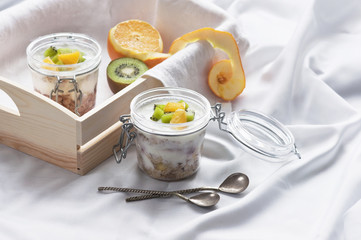 Healthy breakfast of muesli with yogurt and fruit in a glass jar in a tray in bed