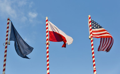 Flags of Nato, Poland and USA outdoor against clear blue sky.