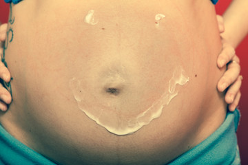 Pregnant woman having cream on big belly