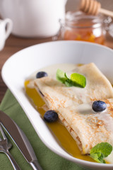 Pancakes with blueberries, mango sauce and coconut, served on a white plate on a wooden table