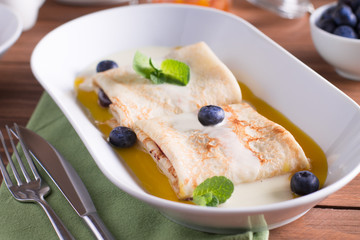 Pancakes with blueberries, mango sauce and coconut, served on a white plate on a wooden table
