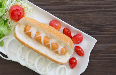 Hotdog with dressing mustard and vegetables in white dish on dark table