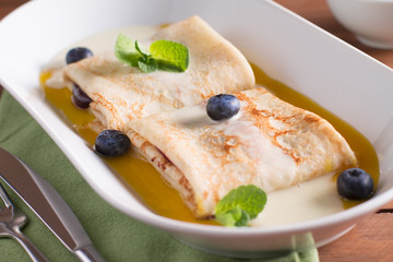 Pancakes with blueberries, mango sauce and coconut, served on a white plate on a wooden table