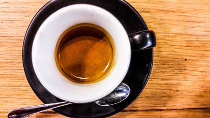Espresso in black coffee cup on wooden surface.