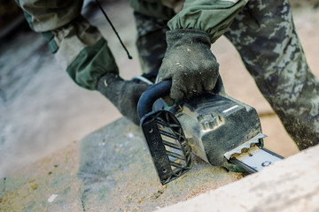 Man in camouflage thick wood saws chainsaw. Flying dust from the drink