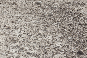 White arid cracked lumpy dry textured desert soil with brown black stones on slope from side 
