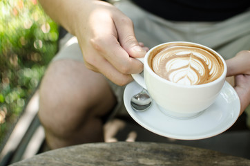 Close up Hand of asia man hold hot Latte Art Coffee in the mug.