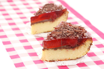 served two slices of delicious cherry cheese cake with cherry topping and decorated with chocolate on checkered tablecloth