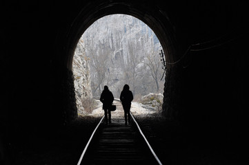 Two women walk the railway and get out from tunnel. Light on the end of the tunnel