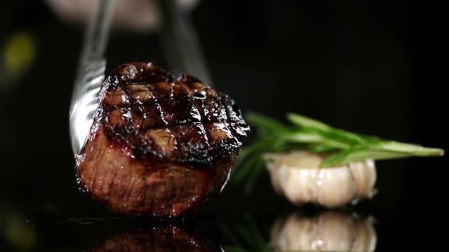 CLOSE UP FOOD: Cooking tongs put filet mignon on a black surface slow motion