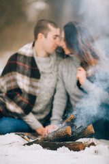 Young woman and man are in front of smoking bonfire in winter picnic.