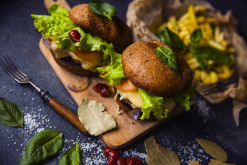 Fast food on the table: burger with beef or pork, or chicken and vegetables, French fries with tomato sauce, basil leaves