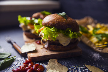 Fast food on the table: burger with beef or pork, or chicken and vegetables, French fries with tomato sauce, basil leaves