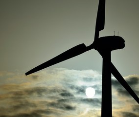 Wind turbine backlit in foreground with sun behind the clouds