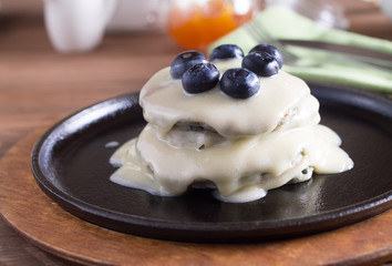 Breakfast, pancakes with maple syrup and fresh berries in a cast iron skillet. Wooden background. Selective focus