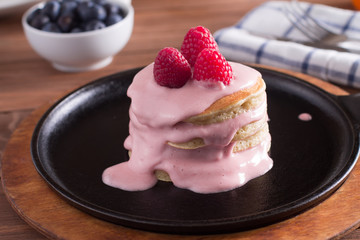 Breakfast, pancakes with maple syrup and fresh berries in a cast iron skillet. Wooden background. Selective focus