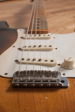 Vintage Fender Stratocaster electric guitar bridge close up with magnets, maple neck and strings in the background on a wooden surface 