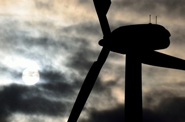 Wind turbine backlit in foreground with sun behind the clouds