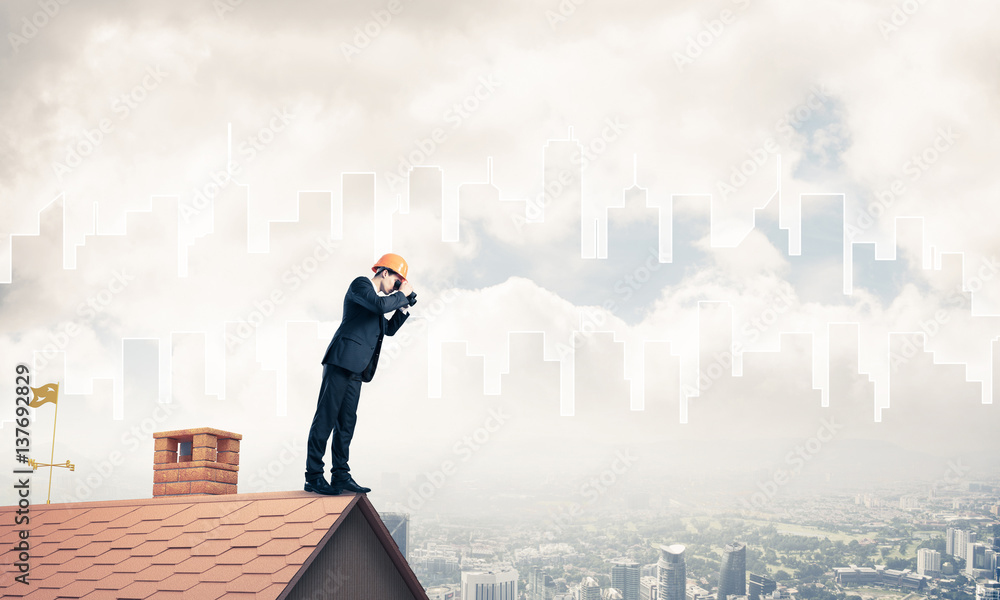 Wall mural Engineer man standing on roof and looking in binoculars. Mixed m