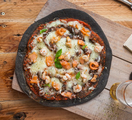 Black pizza with seafood: shrimps, salmon, mussels.