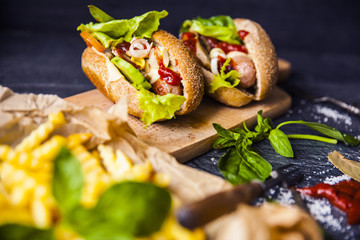 Fast food on the table: hot dog sausage and vegetables, French fries with tomato sauce, basil leaves