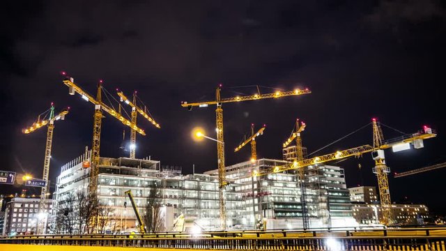 Construction site at night Time Lapse. Working tower cranes, buildings and traffic