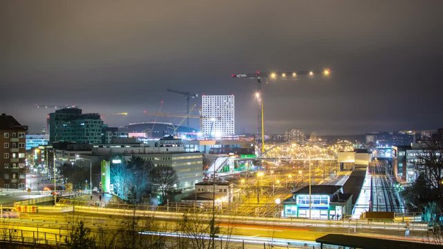 Time Lapse of railroad tracks and construction site at night. Street with traffic and hotel building in the background