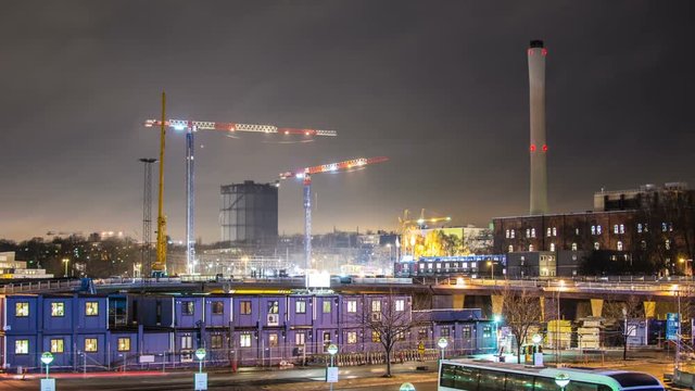 Time Lapse of construction trailers and tower cranes at night. Industrial background, traffic passing by
