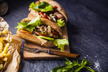 Fast food on the table: hot dog sausage and vegetables, French fries with tomato sauce, basil leaves