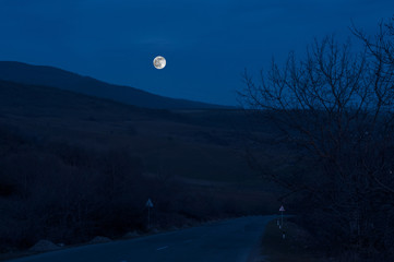 Mountain Road through the forest on a full moon night. Scenic night landscape of dark blue sky with moon. Azerbaijan