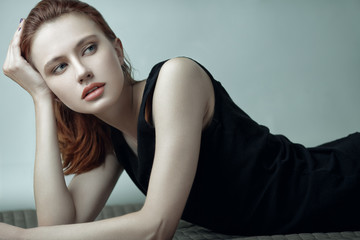 Fashion beauty portrait of young red-haired model with long straight hair in black dress.