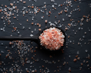 Organic pink salt in wooden spoon on dark background top view