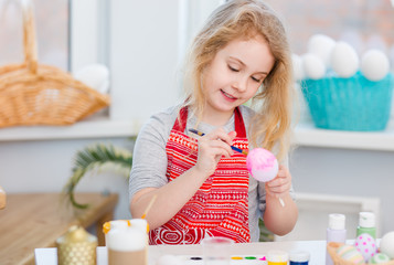 Little blonde girl coloring eggs for Easter holiday at home