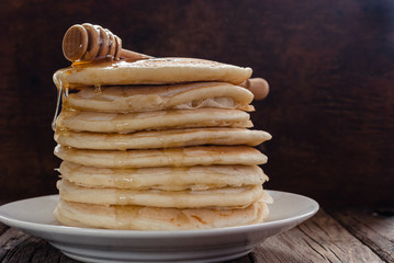 Stack of pancakes with honey on wooden background.